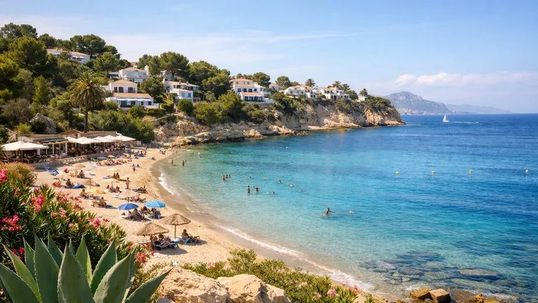 Midday view of a beach in Moraira with the sea, swimmers and a seaside promenade behind